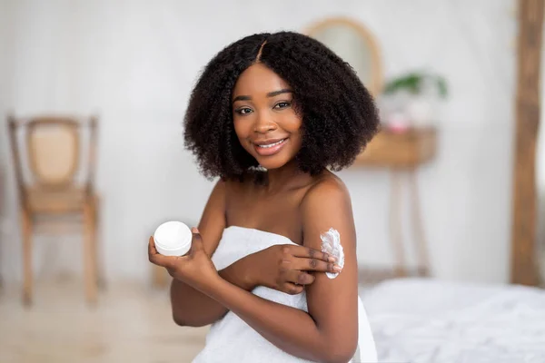 Portret van mooie jonge Afro vrouw genieten van ochtend huidverzorging procedure, het aanbrengen van lichaamscrème thuis — Stockfoto