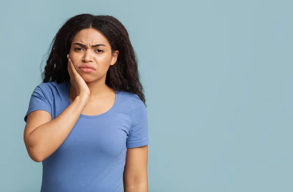 Bolavé zuby. Nešťastná černošky dáma trpí bolestí zubů dotýká tvář přes modré pozadí s volným prostorem — Stock fotografie