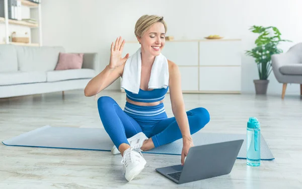 Жінка сидить на йога килимок за допомогою ноутбука махає рукою — стокове фото