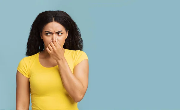 Afrikaans amerikaanse vrouw sluiten neus met vingers, gevoel onaangename geur, staande over blauwe achtergrond, vrije ruimte — Stockfoto