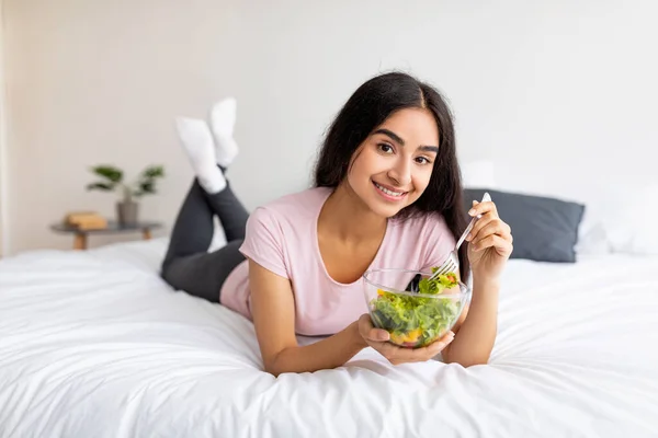 Hälsosam kost, kost och detox koncept. Söt indisk kvinna med färsk vegetarisk sallad, liggande på sängen hemma — Stockfoto