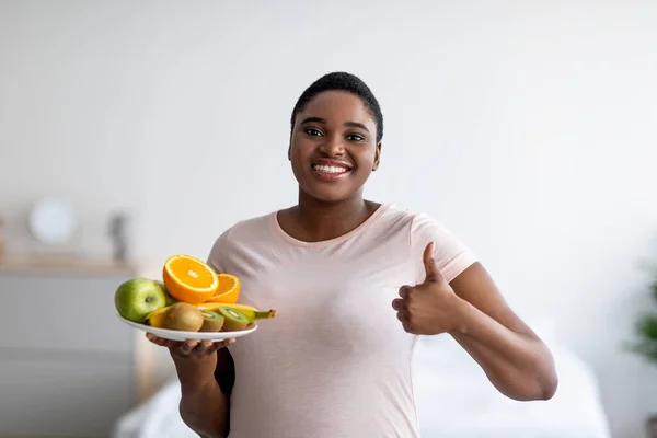 Happy plus size donna nera che tiene i frutti e mostrando pollice in alto, raccomandando una dieta sana per la perdita di peso a casa — Foto Stock