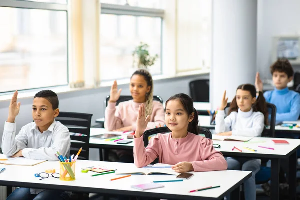 Diverse groepen kleine schoolkinderen steken de hand op in het klaslokaal — Stockfoto
