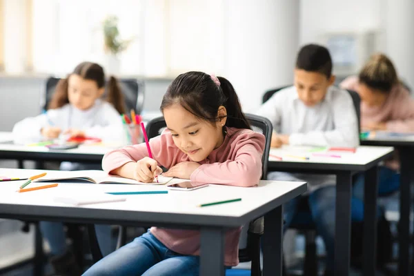 Portrait of diverse schoolchildren sitting in classroom writing and drawing — Stock Photo, Image