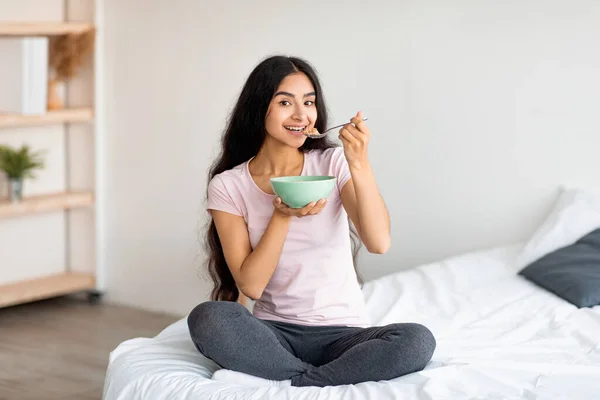 Atraktif wanita India memiliki sereal dengan susu atau jagung sambil duduk di tempat tidur nyaman di rumah — Stok Foto