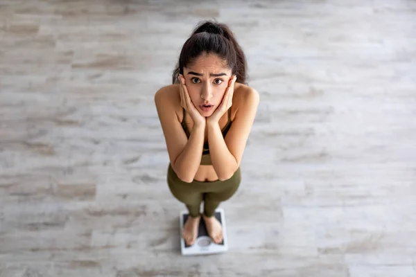 Vue ci-dessus de bouleversé jeune femme indienne debout sur des échelles, se sentant déçu de son résultat de perte de poids — Photo