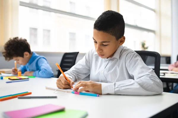 Retrato de niño pequeño sentado en el escritorio y escribiendo —  Fotos de Stock