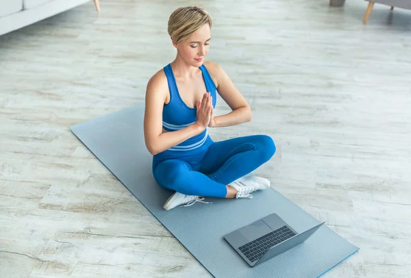 Meditierende Frau sitzt in Lotusposition auf Matte mit PC — Stockfoto