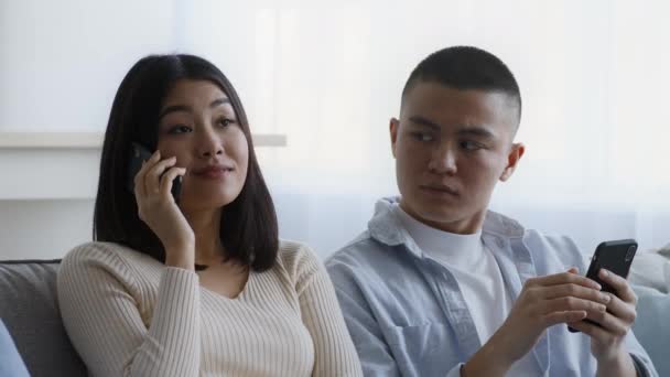 Jaloers aziatische echtgenoot op zoek naar vrouw praten op telefoon indoor — Stockvideo