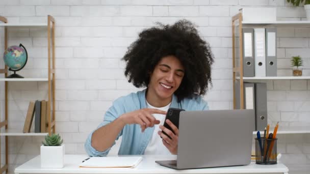 Alegre estudante cara usando smartphone sentado no laptop em casa — Vídeo de Stock