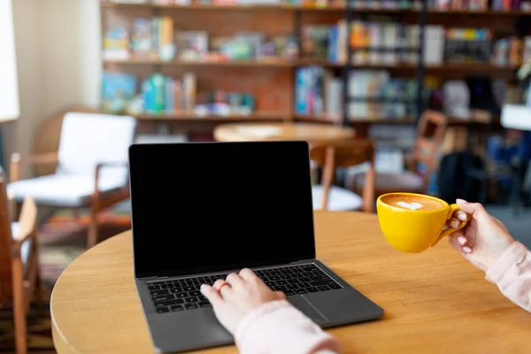 Femeie tânără tastând pe tastatura laptopului, folosind computerul cu ecran gol și bând cafea, stând în cafenea — Fotografie, imagine de stoc