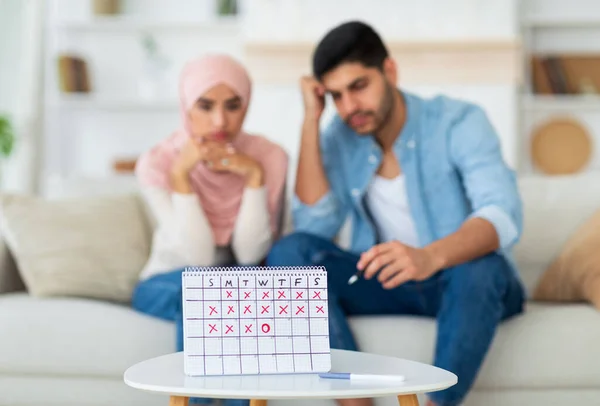 Giovane musulmano pianificazione familiare gravidanza, seduto sul divano e guardando calendario ovulazione, messa a fuoco selettiva — Foto Stock