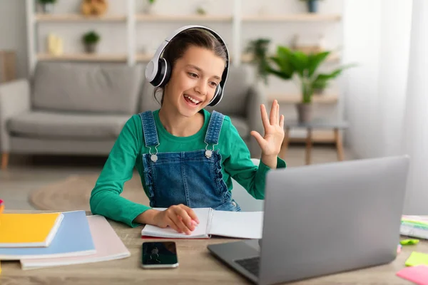 Menina sentada à mesa, usando laptop, acenando para webcam — Fotografia de Stock