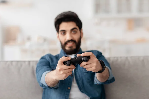 周末休闲。快乐的阿拉伯人，用操纵杆玩网络游戏，坐在客厅的沙发上 — 图库照片