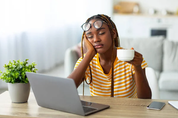 Wyczerpany czarny kobieta siedzi przed laptopem, pije kawę — Zdjęcie stockowe