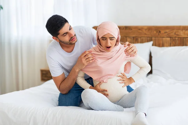 Prenatale weeën. Zwangere moslim vrouw die lijdt aan buikpijn en zorgzame Arabische man troostende vrouw — Stockfoto