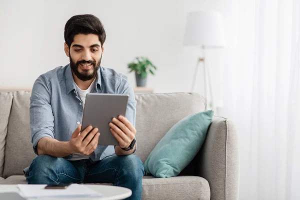 Koncept volného času. Portrét šťastného chlapa s digitálním tabletem, sedící doma na gauči, volné místo — Stock fotografie