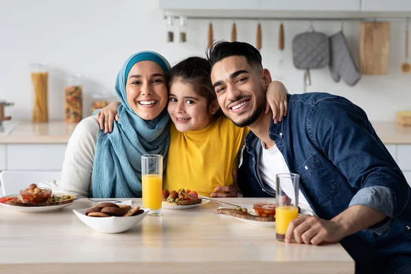 Aranyos kis arab lány átöleli a szüleit, miközben együtt ebédelnek. — Stock Fotó