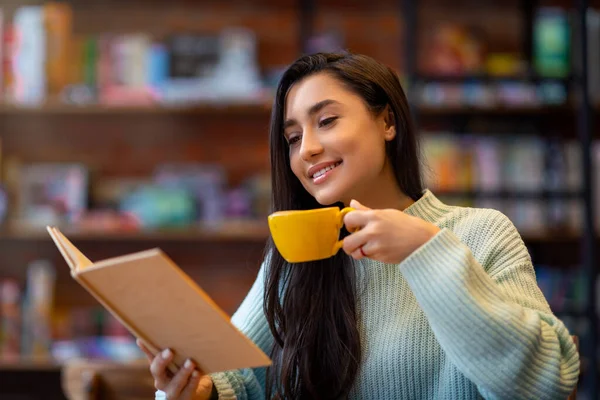 Joven señora árabe leyendo libro favorito y disfrutando del café en la cafetería, sentado en la cafetería y pasar tiempo con placer — Foto de Stock