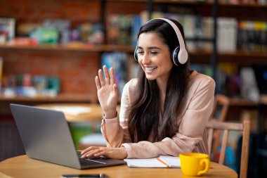 Cafe 'de dinlenirken görüntülü konuşma yapan neşeli Latin kadın, dizüstü bilgisayar ve kulaklık kullanıyor, boşluğu kopyalıyor