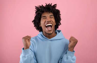 Büyük galibiyet, büyük şans. Yakışıklı Afrikalı Amerikalı genç EVET hareketi yapıyor, pembe stüdyo arka planında OMG diye bağırıyor.