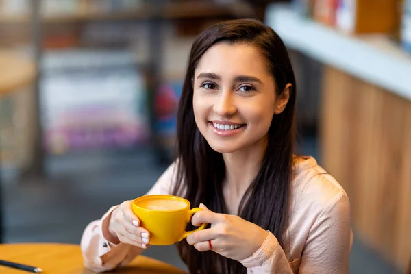 Koffie tijd. Portret van een gelukkige Arabische vrouw met een mok warme drank, rustend in een café en kijkend naar de camera, vrije ruimte — Stockfoto