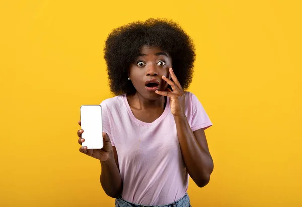 충격적 인 모바일 뉴스 컨셉. 감정적 인 흑인 여성 이 노란 배경 위에 빈 화면 이 있는 스마트폰을 보여 주고 있다 — 스톡 사진