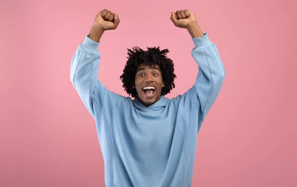 Triunfante negro adolescente chico levantando brazos por encima de su cabeza, gritando en la emoción en rosa estudio fondo —  Fotos de Stock