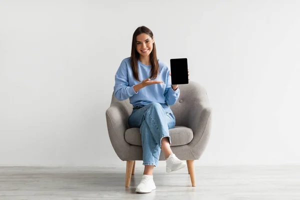Ευτυχισμένη κυρία που δείχνει φορητό υπολογιστή με κενή οθόνη για την ιστοσελίδα, παρουσιάζοντας touch pad με mockup, κάθεται στην πολυθρόνα — Φωτογραφία Αρχείου