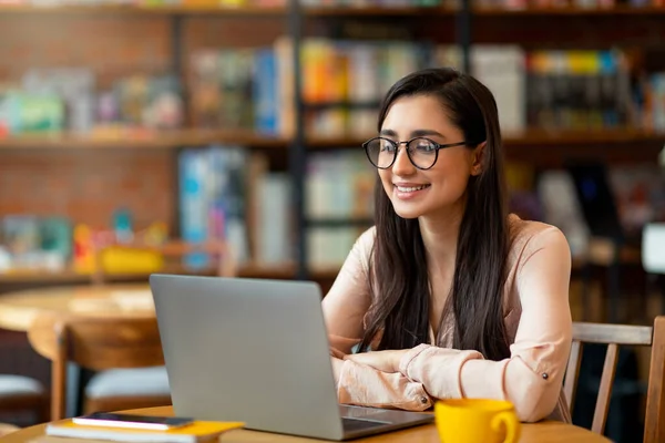 Senhora latina alegre trabalhando on-line no café, usando laptop e beber café ou chá, espaço livre — Fotografia de Stock