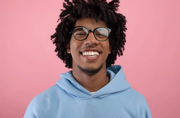 Portrét radostného černošky teenager s příjemným úsměvem nosí brýle, při pohledu na kameru na růžové pozadí studia — Stock fotografie