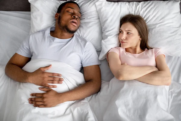 Top kilátás irritált fiatal nő bosszús a fekete férje horkolás az ágyban — Stock Fotó