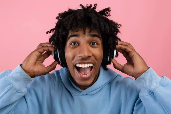 Overhappy zwart tiener genieten van populaire muziek in headset, opening mond in opwinding op roze achtergrond — Stockfoto