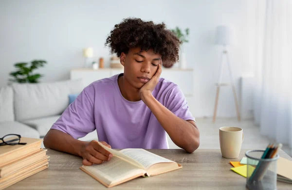 疲惫的黑人少年坐在书桌前，看书，在家学习 — 图库照片