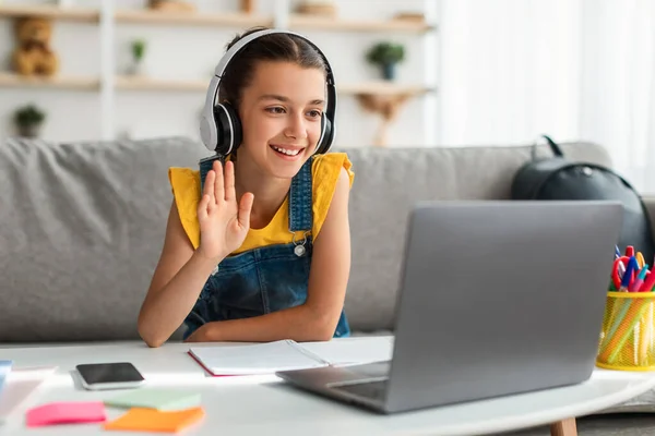 Girl in headphones using laptop, waving to webcam — Stock Photo, Image