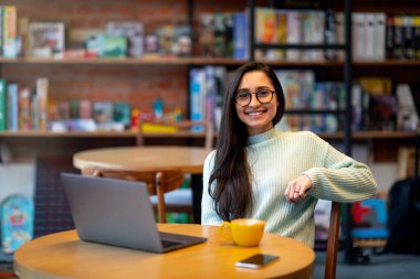 Kafede oturup dizüstü bilgisayar ve boş alan kullanırken uzaktan çalışan heyecanlı Arap kadın serbest yazar.