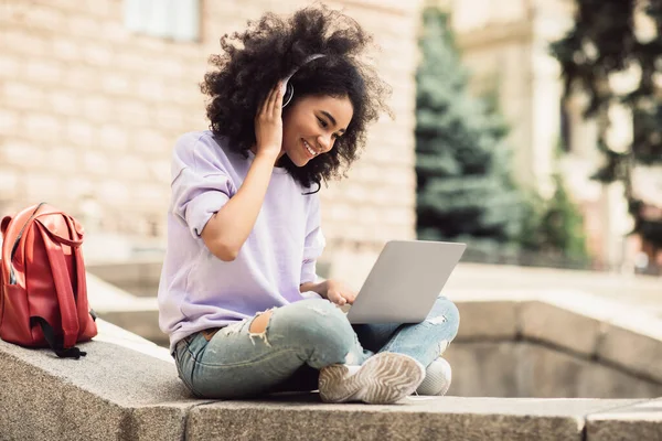 Estudiante femenina negra usando el ordenador portátil que tiene una conferencia en línea sentada al aire libre — Foto de Stock