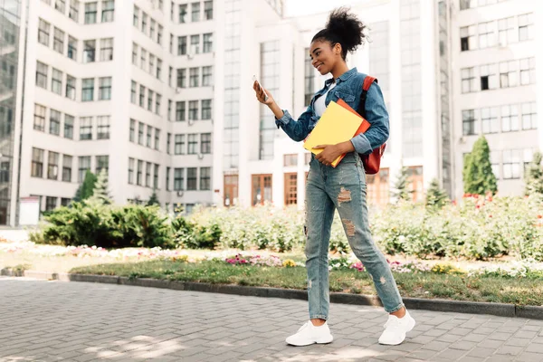 Afroamerikansk studentjente som bruker Smartphone Browsing Internett stående utendørs – stockfoto