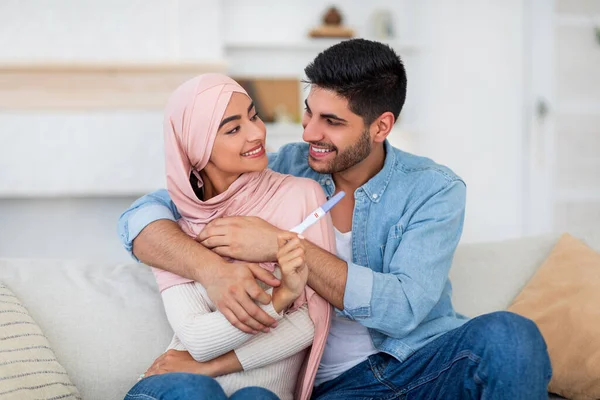 Sorpresa e futuri genitori. Felice giovani coniugi musulmani che tengono test di gravidanza positivi e si sorridono a vicenda — Foto Stock