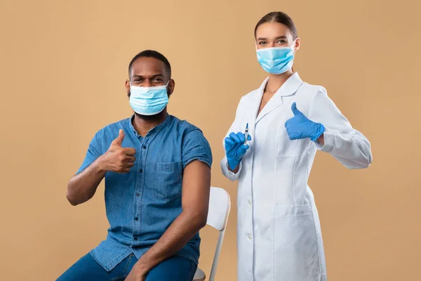 Trabajador médico y paciente varón negro vacunado mostrando pulgares hacia arriba, recomendando inmunización contra el coronavirus —  Fotos de Stock