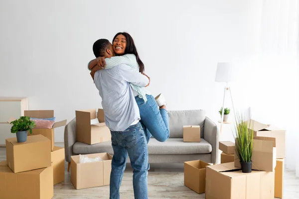 Домовладельцы. Счастливый африканский американец обнимает и поднимает жену, празднует день переезда в своей квартире, свободное место — стоковое фото