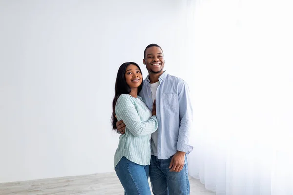 House ownership. Loving african american couple embracing and smiling, standing in empty room of their new apartment — Stock Photo, Image