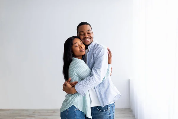 Young loving african american couple moving to new apartment, embracing while standing in empty room, free space — Stock Photo, Image