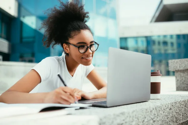 Felice nero studente ragazza fare i compiti a casa utilizzando computer portatile all'aperto — Foto Stock