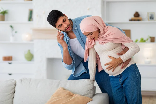 Terhes muszlim nő, akinek prenatális összehúzódások, gondoskodó férj hívja orvos okostelefon, szabad hely — Stock Fotó