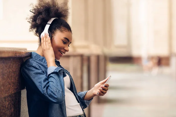 Noir étudiant fille en utilisant Smartphone port casque écouter de la musique en plein air — Photo