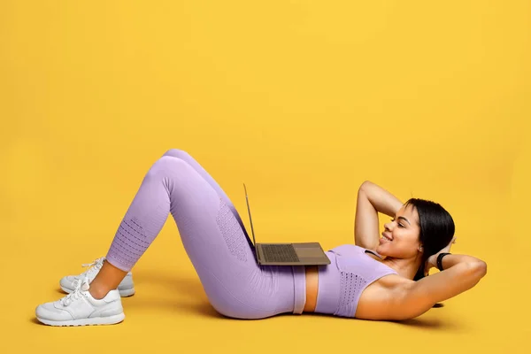 Palestra online. Adatta donna afro-americana che fa addominali esercizio sit-up, formazione con il computer portatile, esercizio su sfondo giallo — Foto Stock