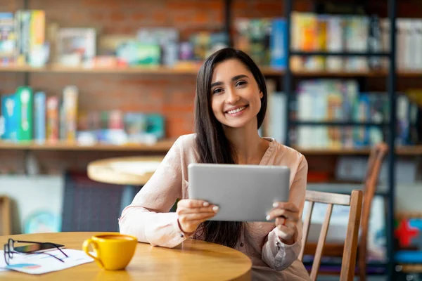 카페에 앉아 디지털 태블릿을 사용하고 커피를 마시며 카메라 앞에서 웃고 복사하는 행복 한 아라파 여성 — 스톡 사진
