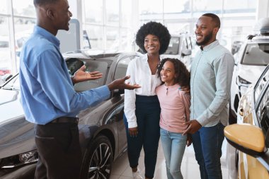 Araba satma işi. Otomobil galerisindeki siyahi aileye lüks otomobil gösteren kendine güvenen bir yönetici.