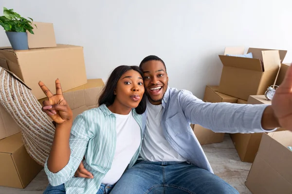 Gelukkige huiseigenaren. jong Afrikaans Amerikaans paar nemen selfie na het verhuizen naar een nieuw huis, zittend tussen kartonnen dozen — Stockfoto